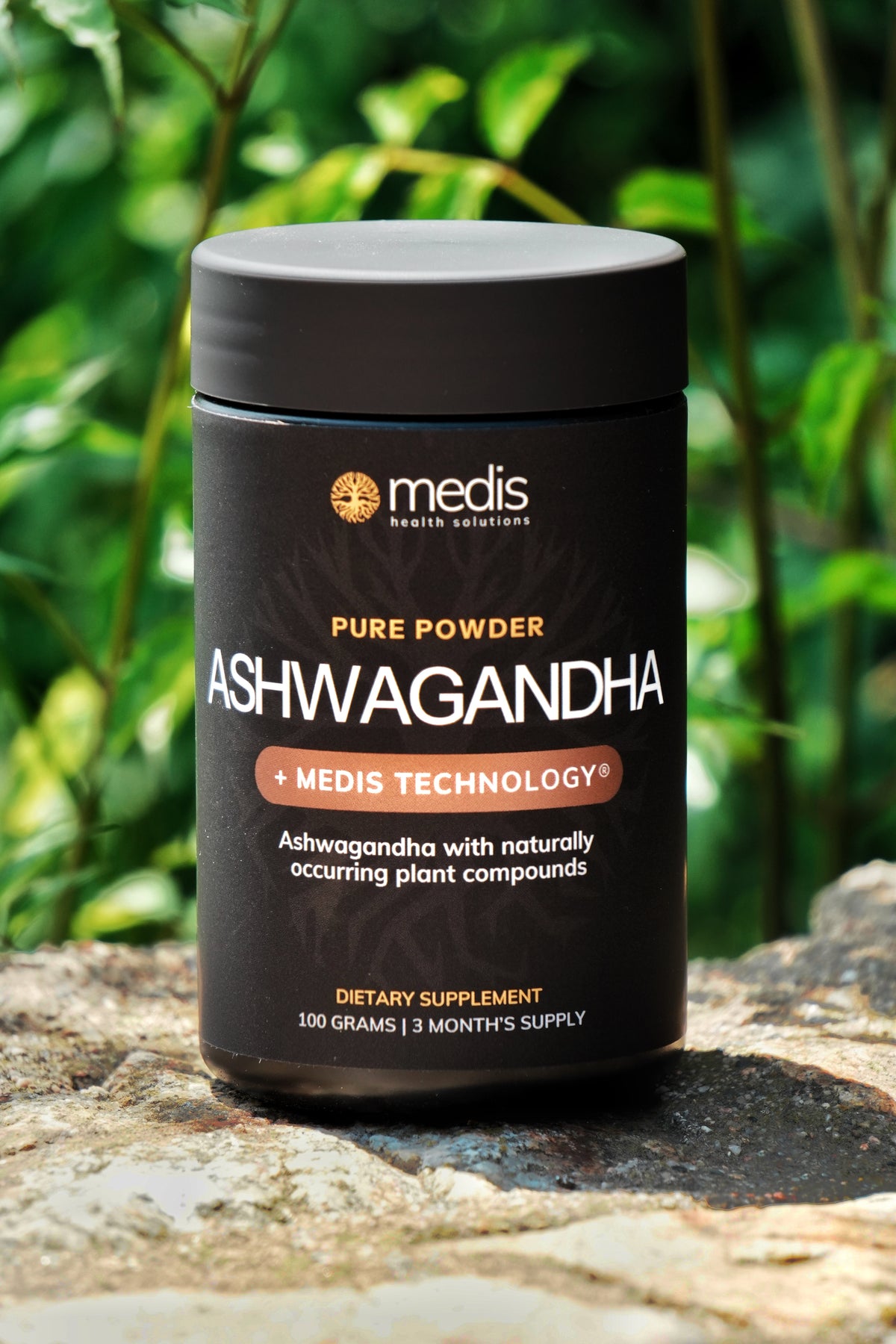 A black bottle of Medis Ashwagandha pure powder dietary supplement, set outdoors on a stone surface with a blurred green garden background.