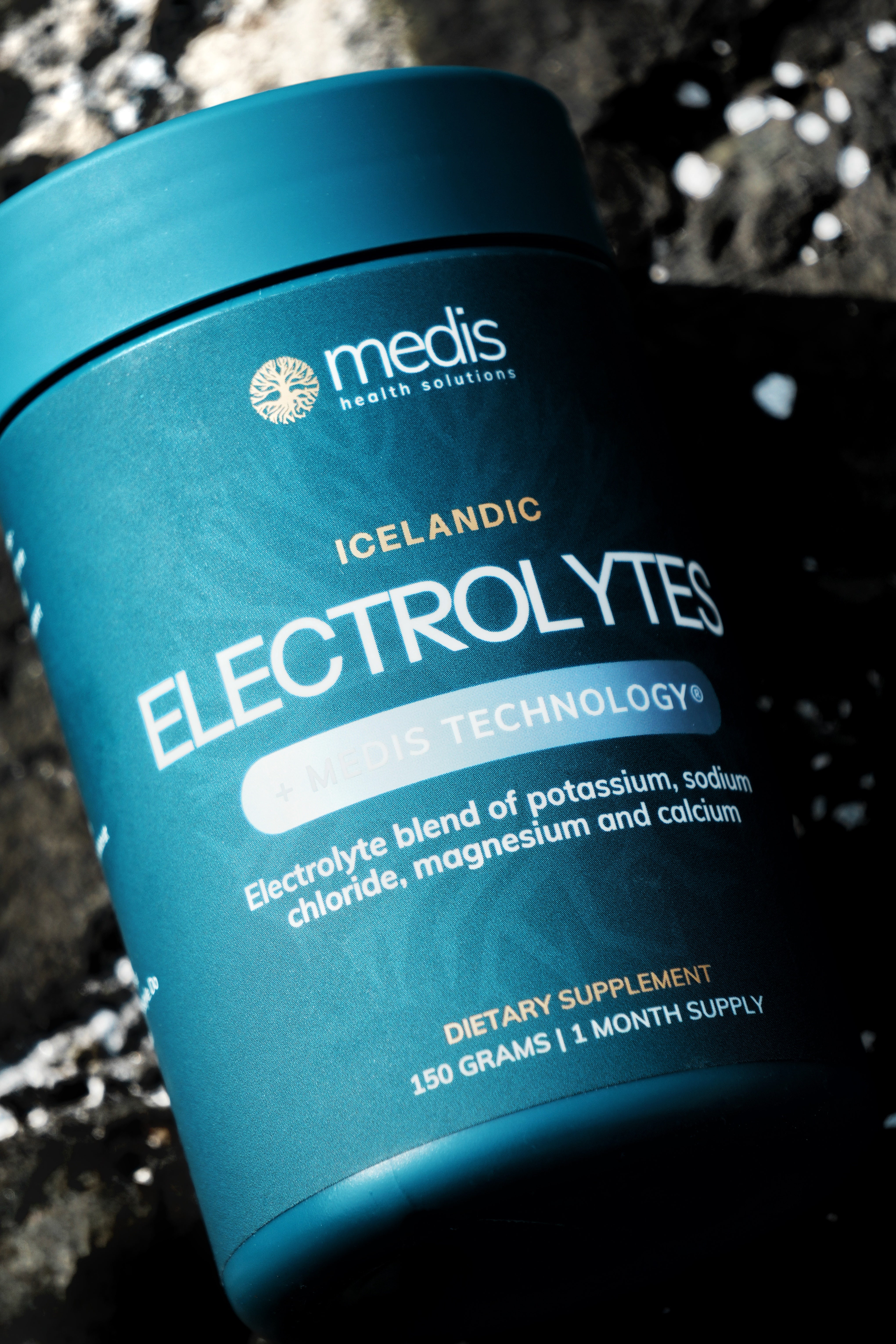 A teal blue container of Medis Health Solutions Icelandic Electrolytes dietary supplement, photographed at an angle against a dark, textured stone background.