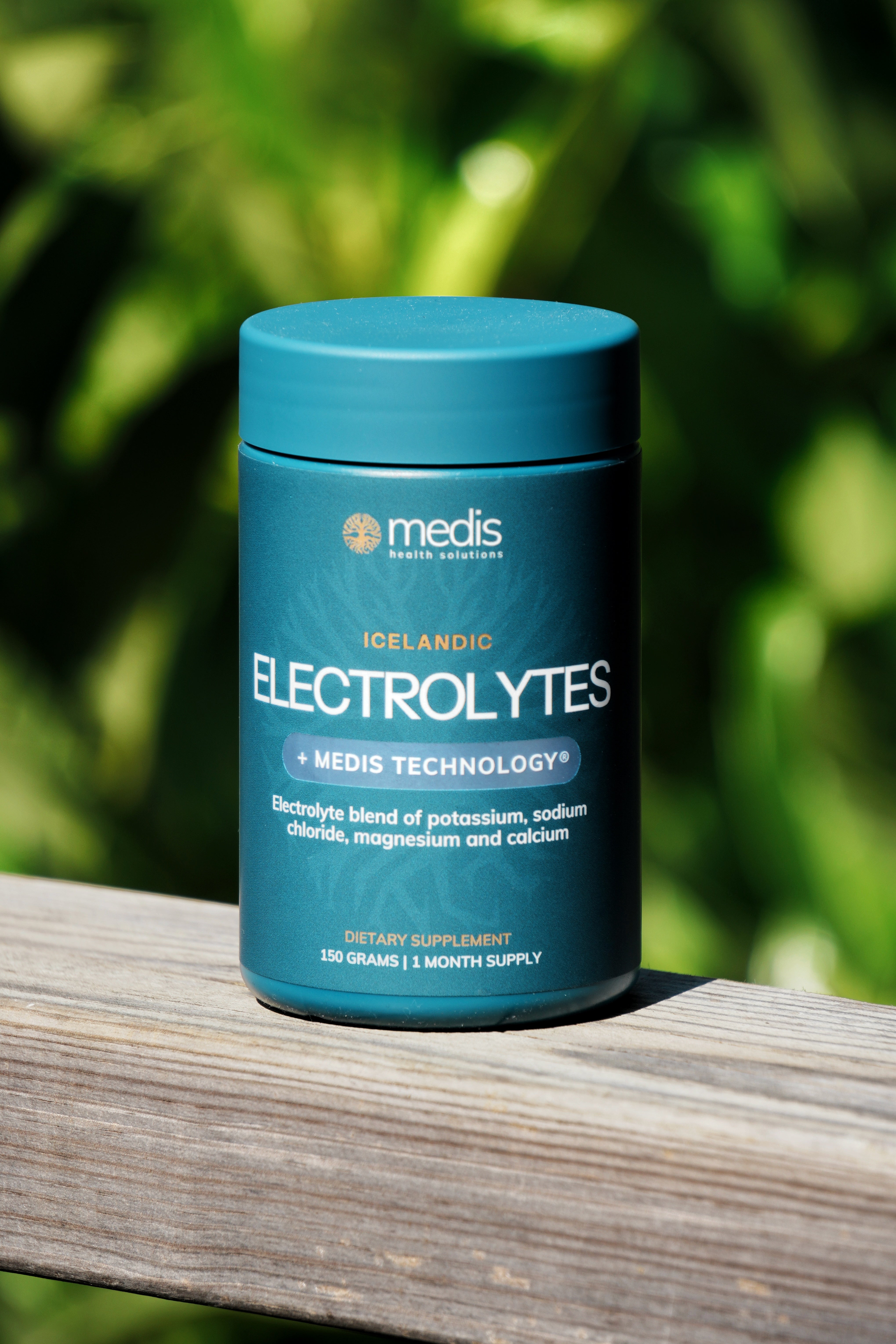 A teal blue jar of Medis Icelandic Electrolytes dietary supplement, placed on a weathered wooden surface with a blurred green garden background.