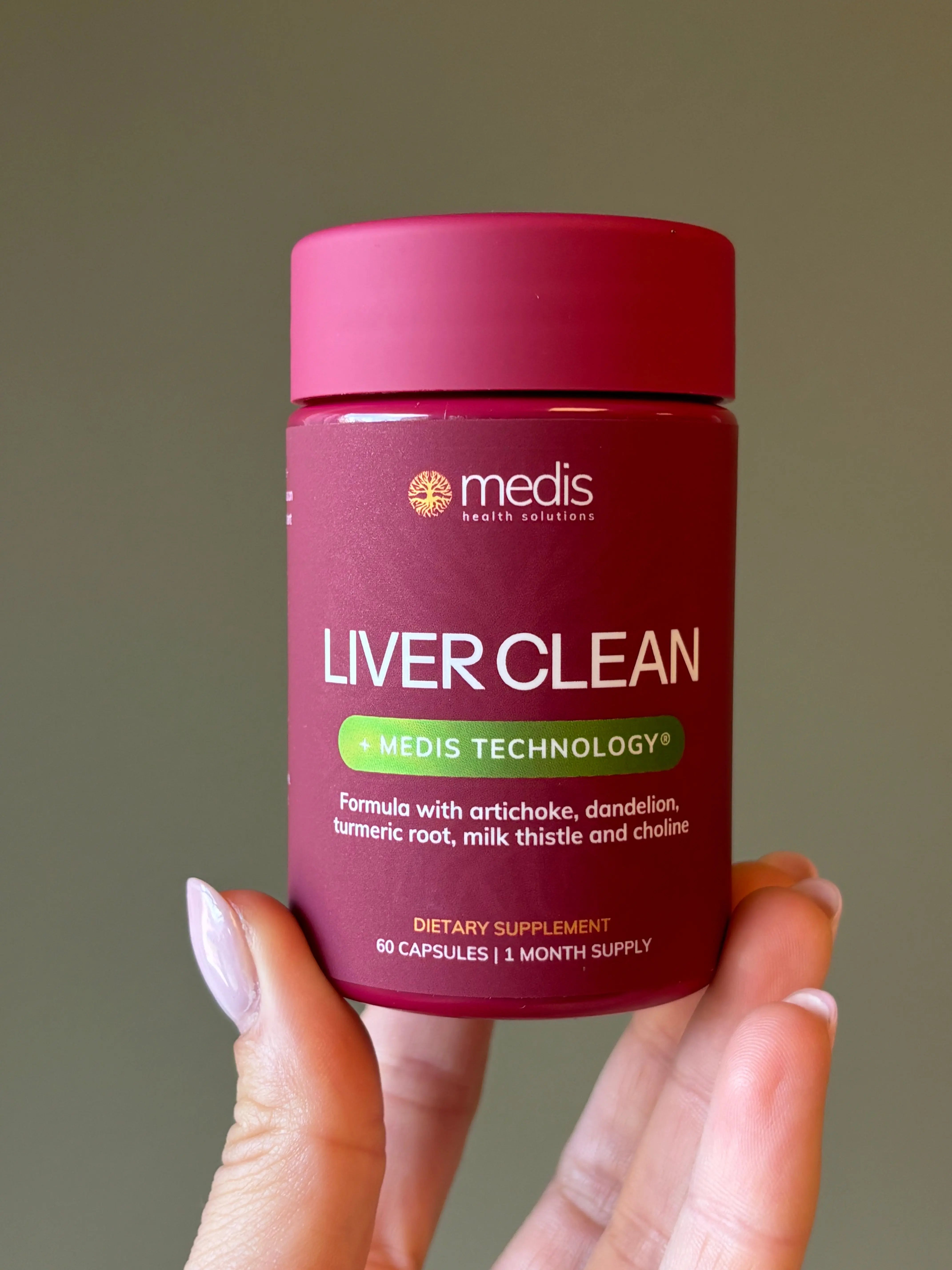 A hand holding a magenta bottle of Medis Liver Clean dietary supplement against a solid olive-gray background.